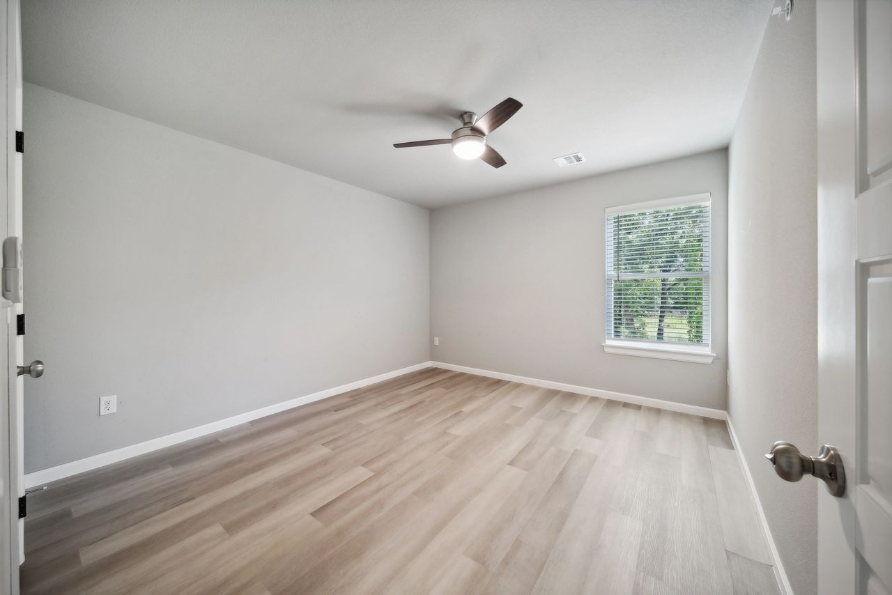 Empty room with light gray walls, wood-look flooring, a ceiling fan, and a window with a view.