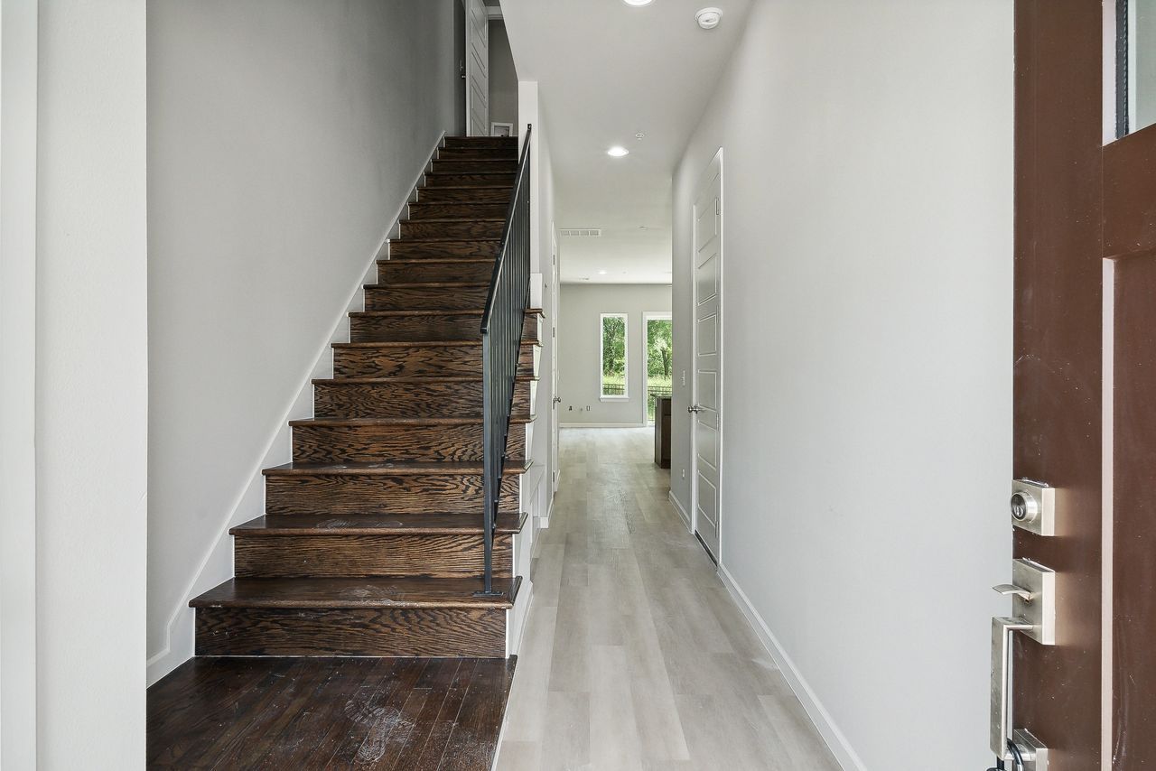 A modern entryway with wooden stairs, light wood floors, and white walls.