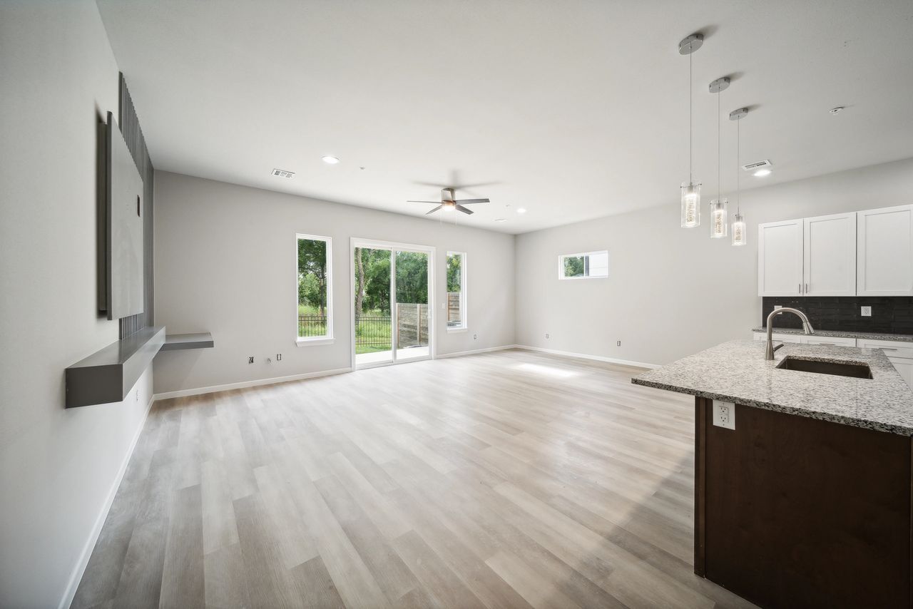 Empty modern living space with wood floors, kitchen island, and sliding glass doors.