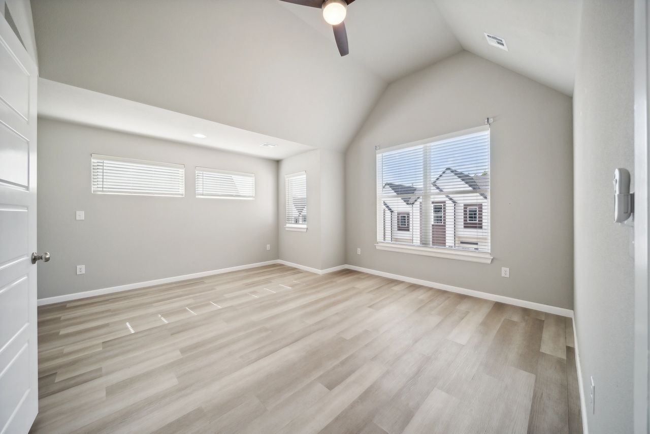 Empty bedroom with wood-look flooring, gray walls, and a large window looking out at houses.