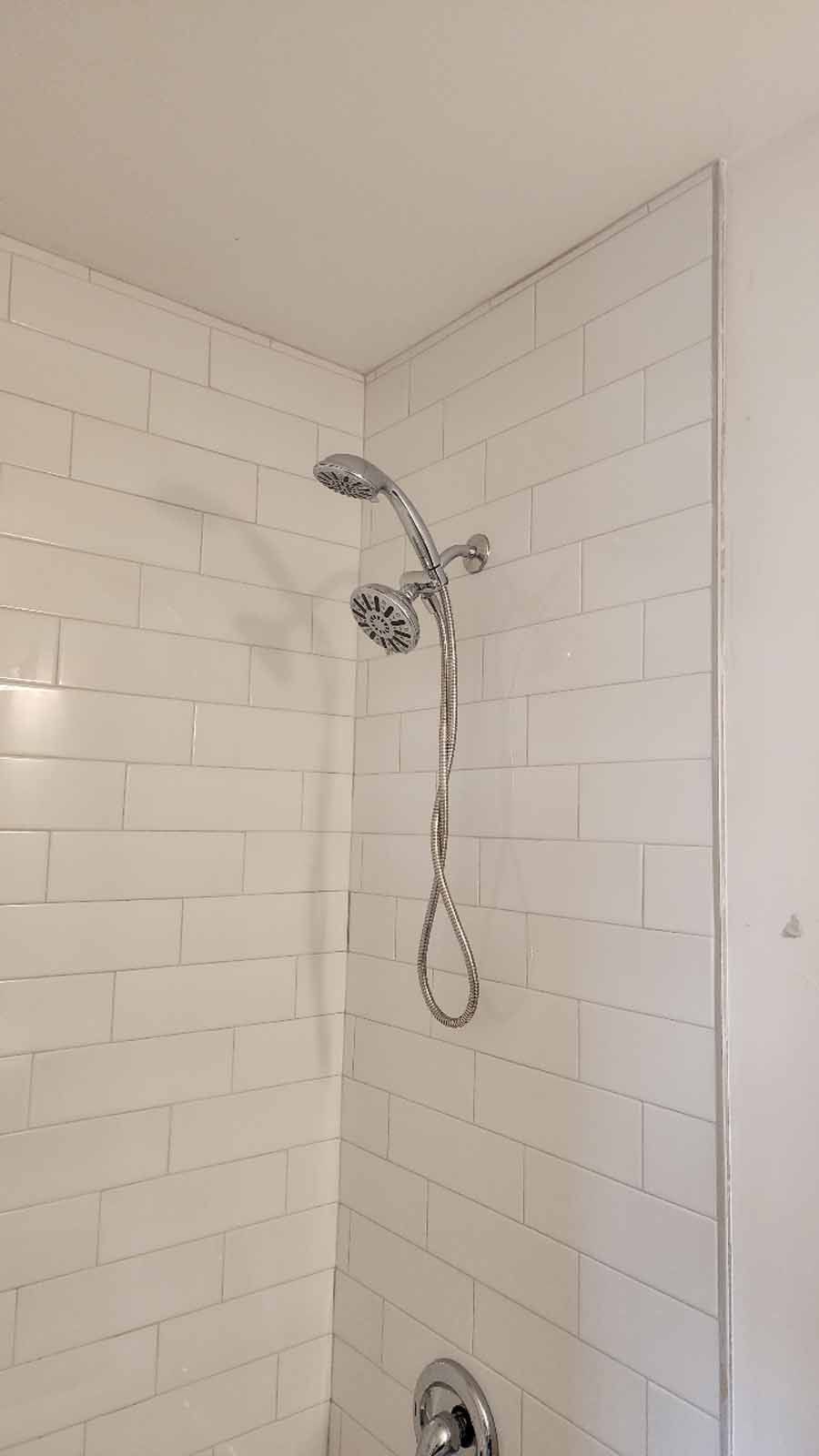 White tiled shower with a dual showerhead and chrome fixtures.