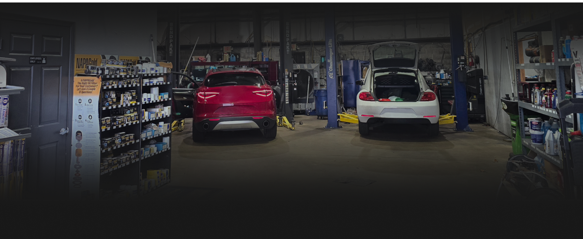 Inside a garage, a red car and a white car are being worked on.  | Integrity Auto Repair