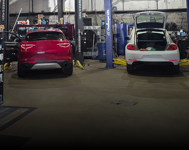 An auto repair shop with two cars on lifts. Shelves with parts line the walls.  | Integrity Auto Repair