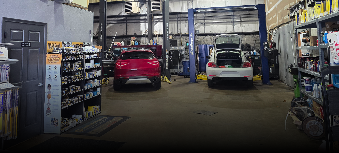 Inside a car repair shop, two cars between auto lifts, shelves of parts, open doors.  | Integrity Auto Repair