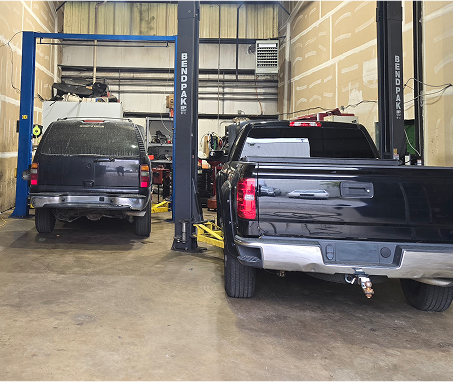 Two black vehicles inside an auto repair shop, on lifts.  | Integrity Auto Repair
