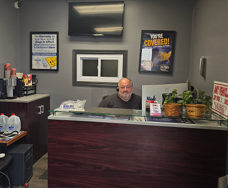 A man at a desk inside an auto shop. He has a gray beard and is wearing a gray shirt.  | Integrity Auto Repair