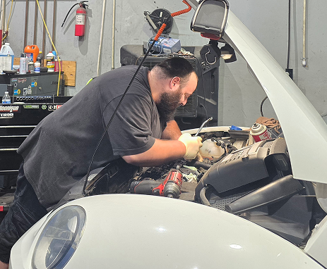 Mechanic working on a white car engine in a garage. He's wearing gloves and using tools.  | Integrity Auto Repair