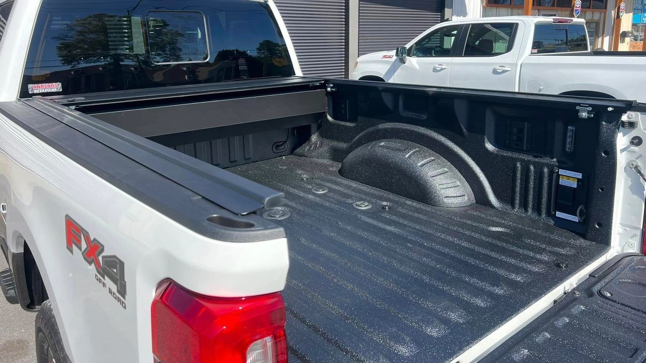 A white pickup truck is parked next to a black pickup truck.