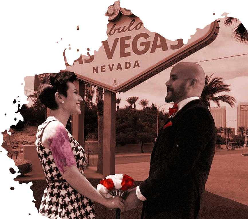 Couple holding hands, smiling in front of the Las Vegas sign. Bride in black and white dress, groom in suit, holding flowers.