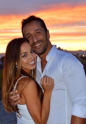 Couple embracing, smiling at sunset. Man in white shirt, woman in white dress.