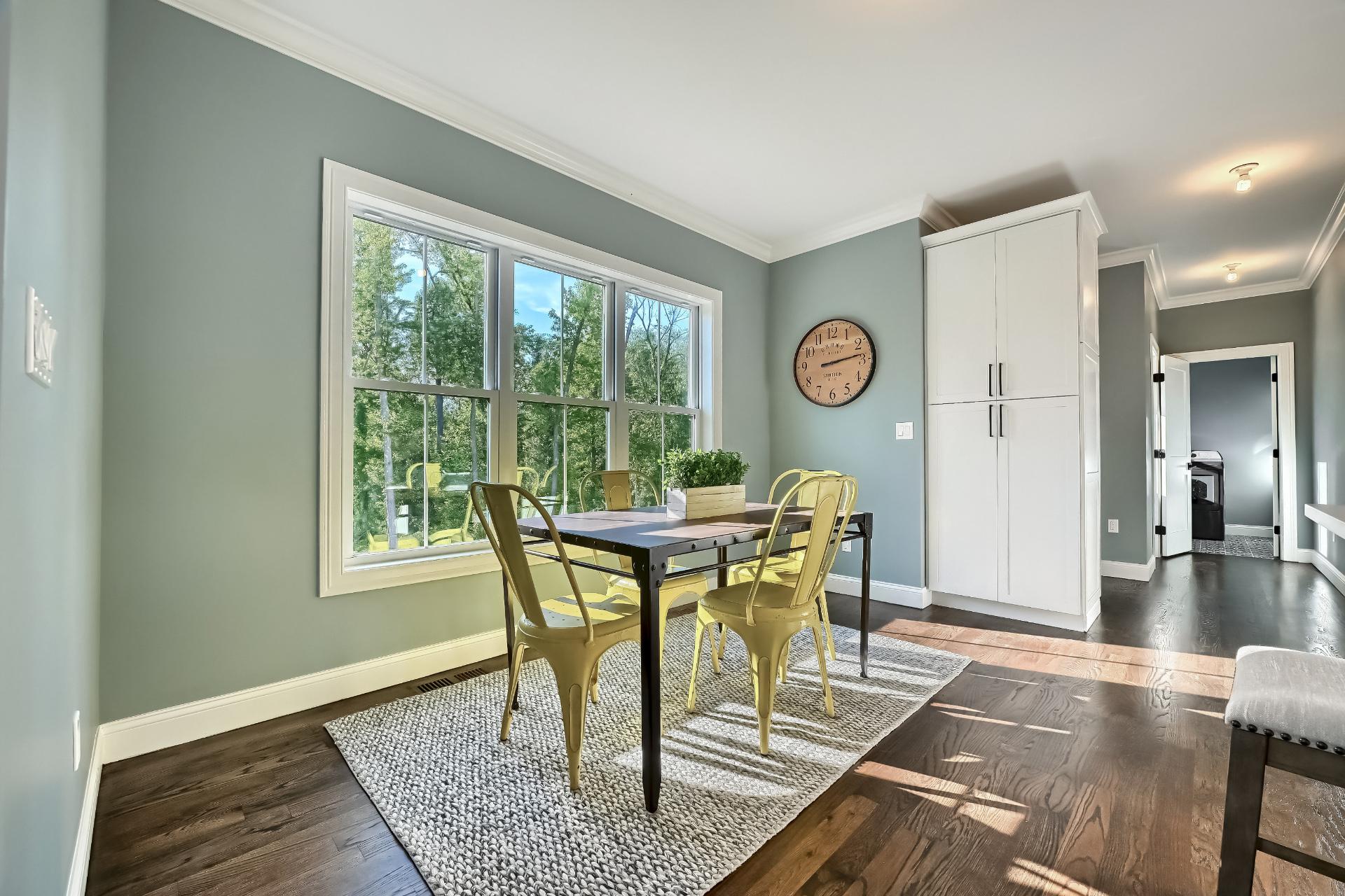 A dining room with a table and chairs and a clock on the wall.