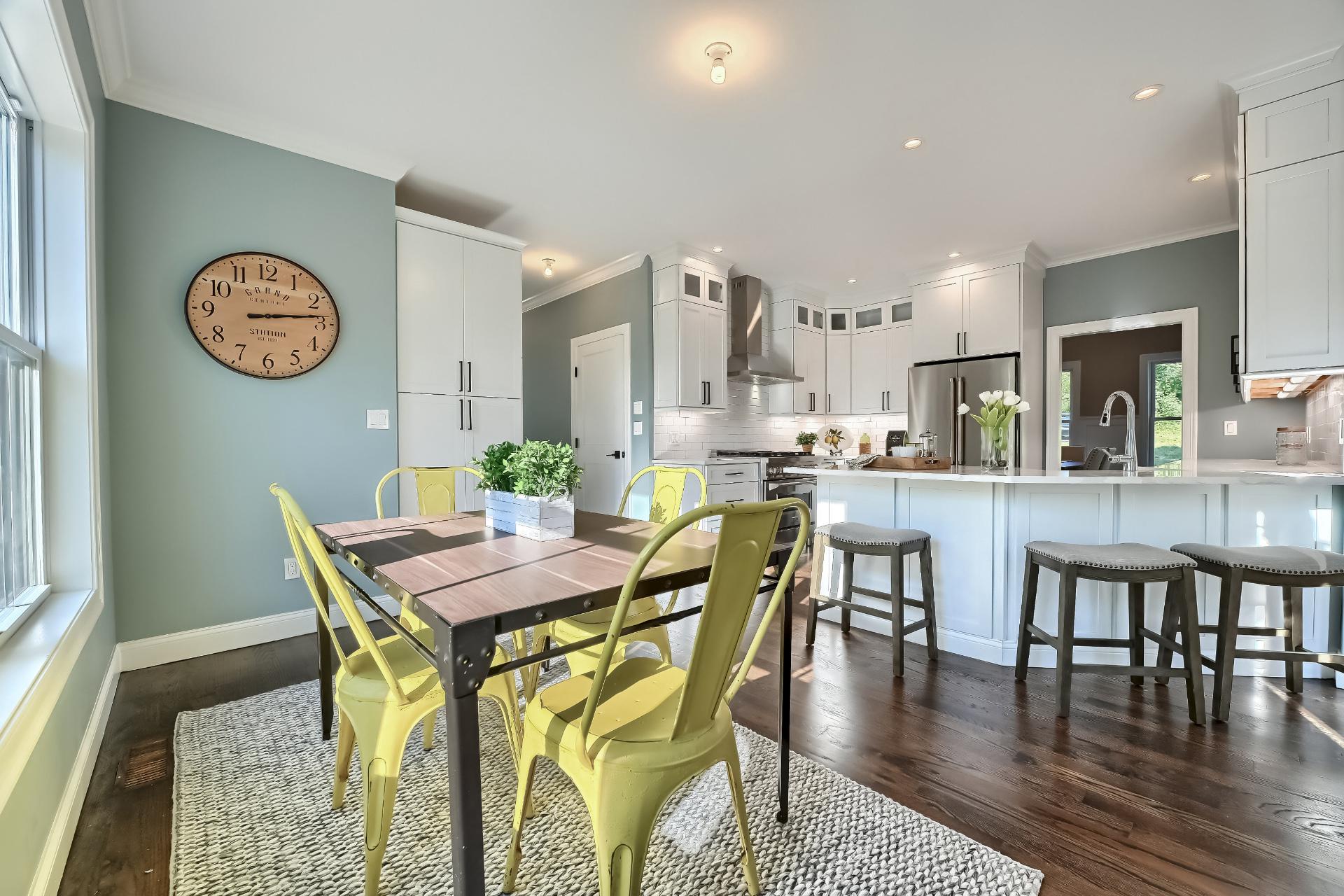 A dining room with a table and chairs and a clock on the wall.