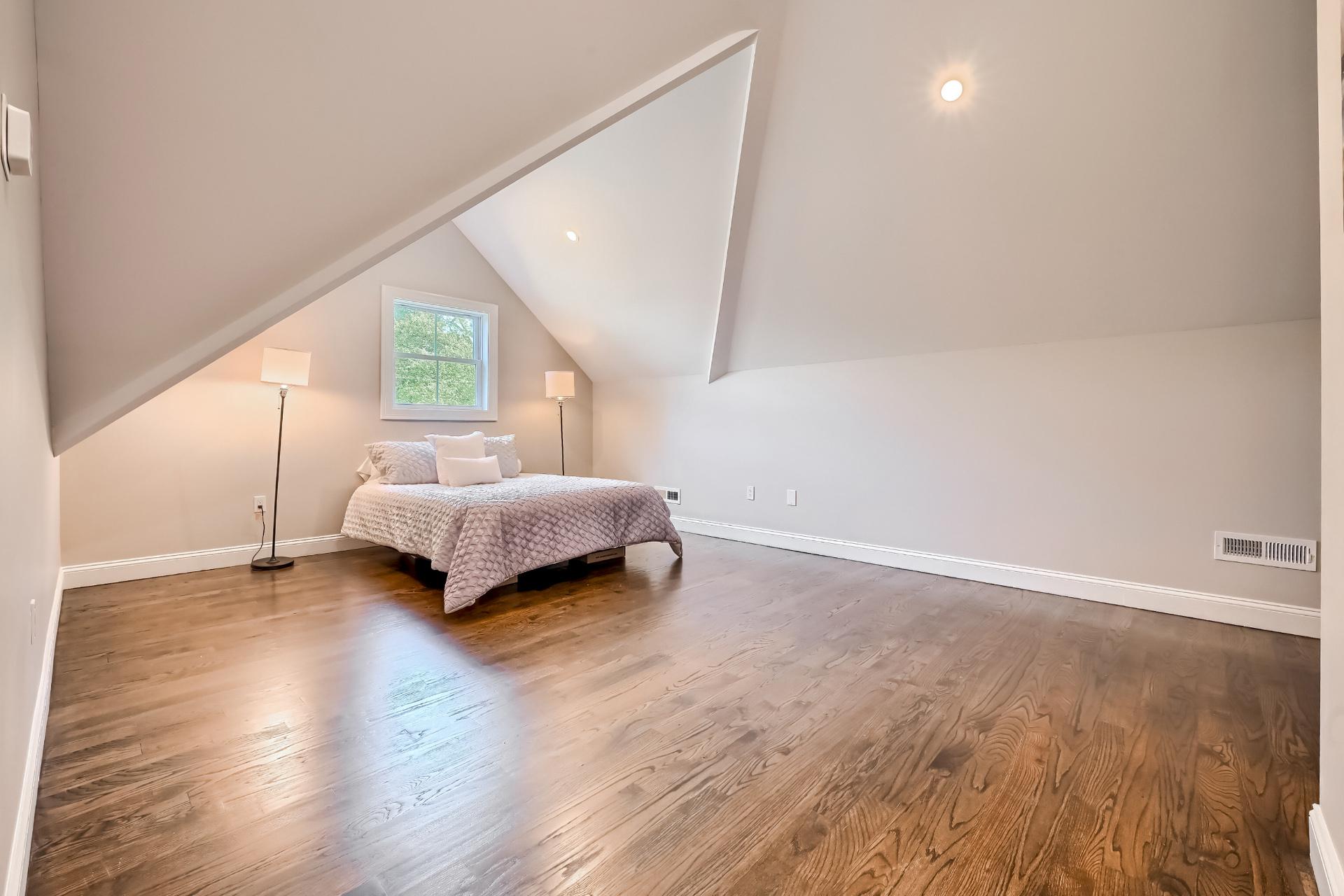 A bedroom with hardwood floors and a bed in the attic.