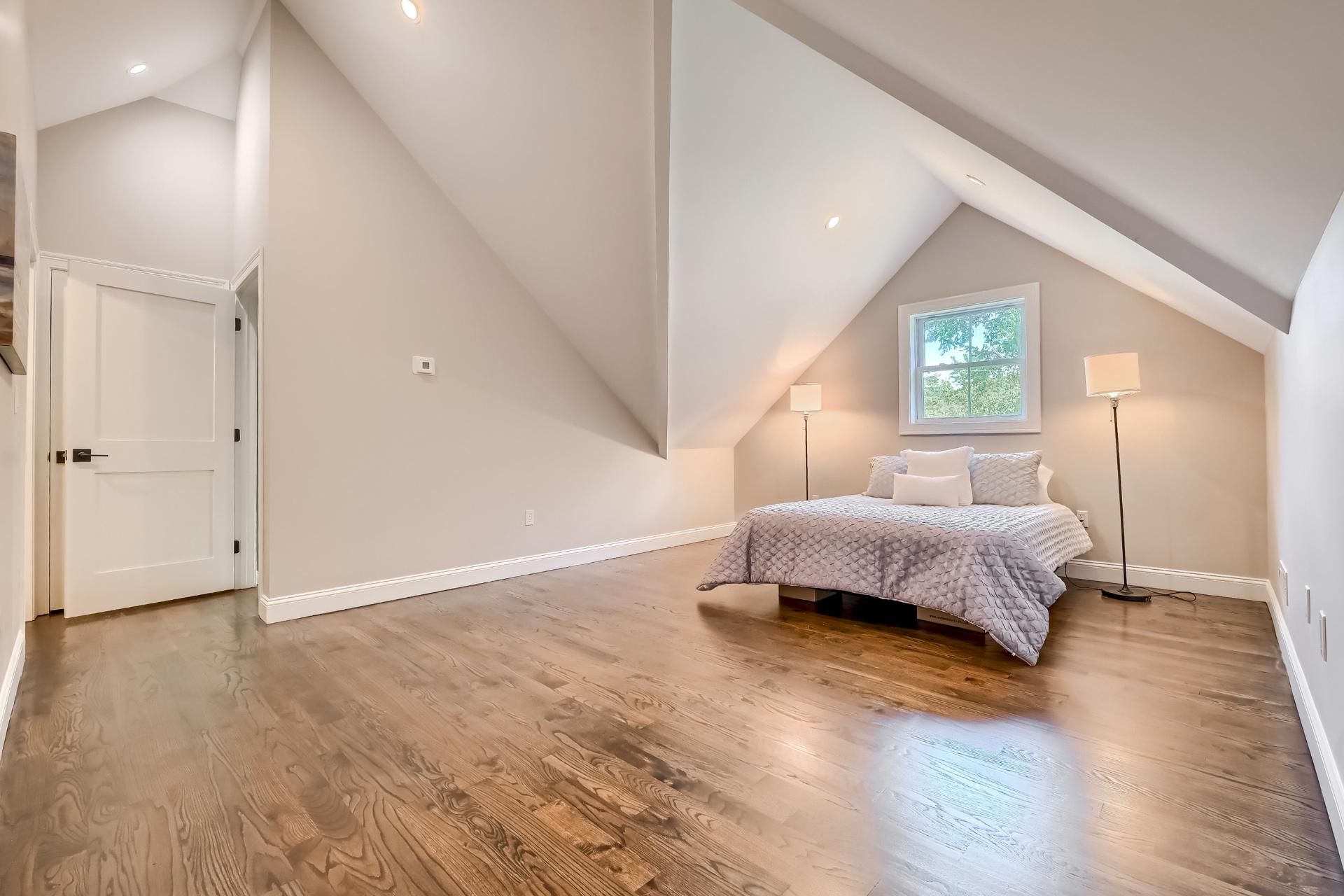 A bedroom with hardwood floors and a bed in the attic.
