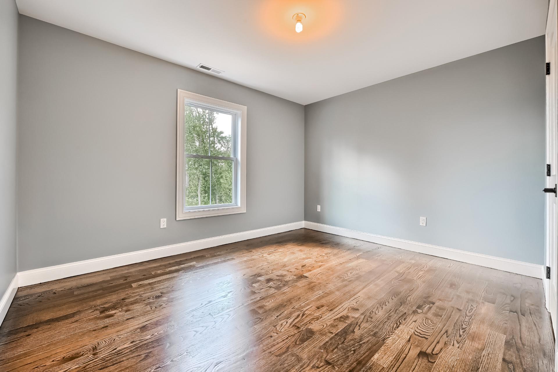 An empty bedroom with hardwood floors and gray walls.