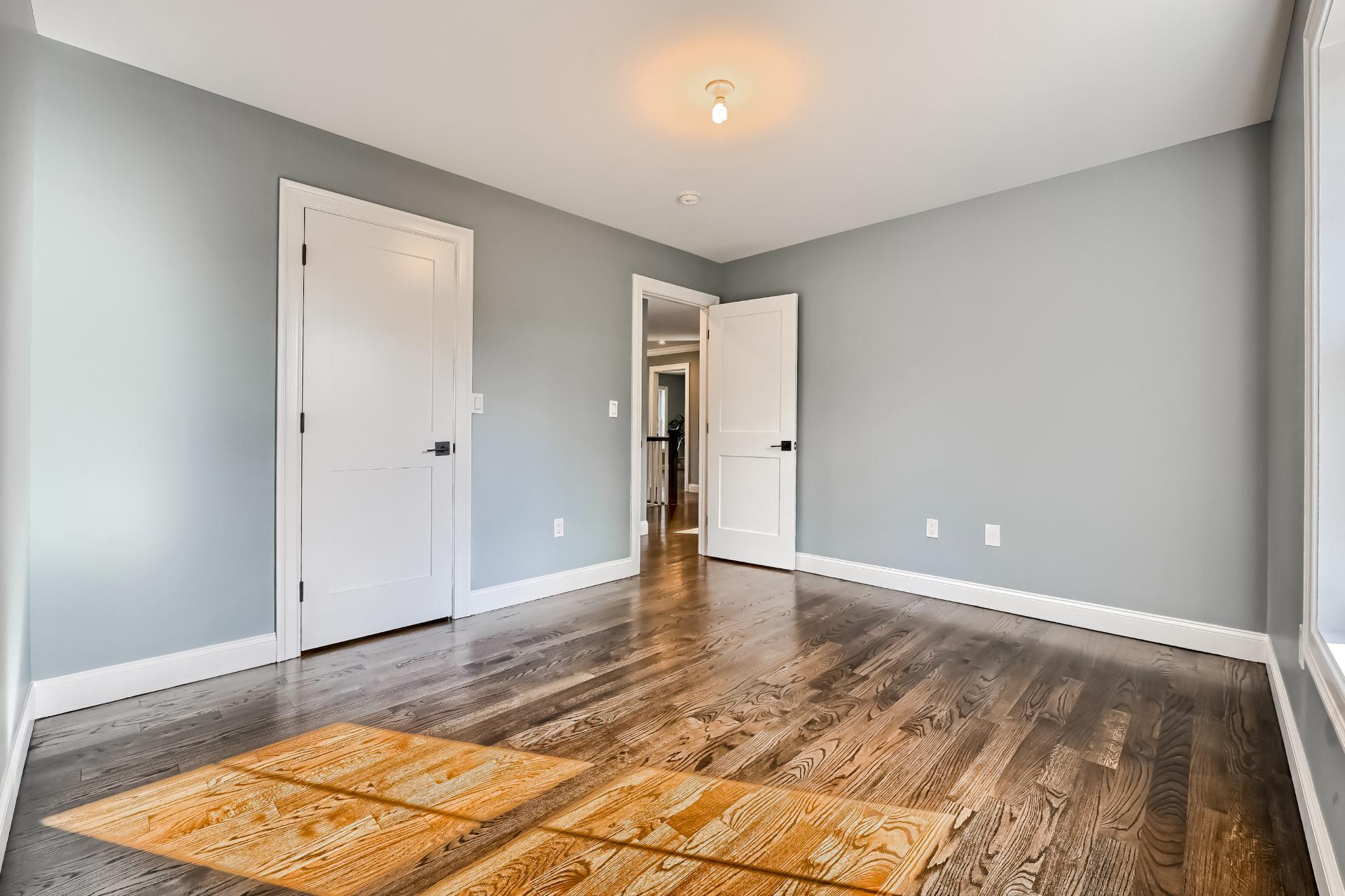 An empty bedroom with hardwood floors and gray walls.