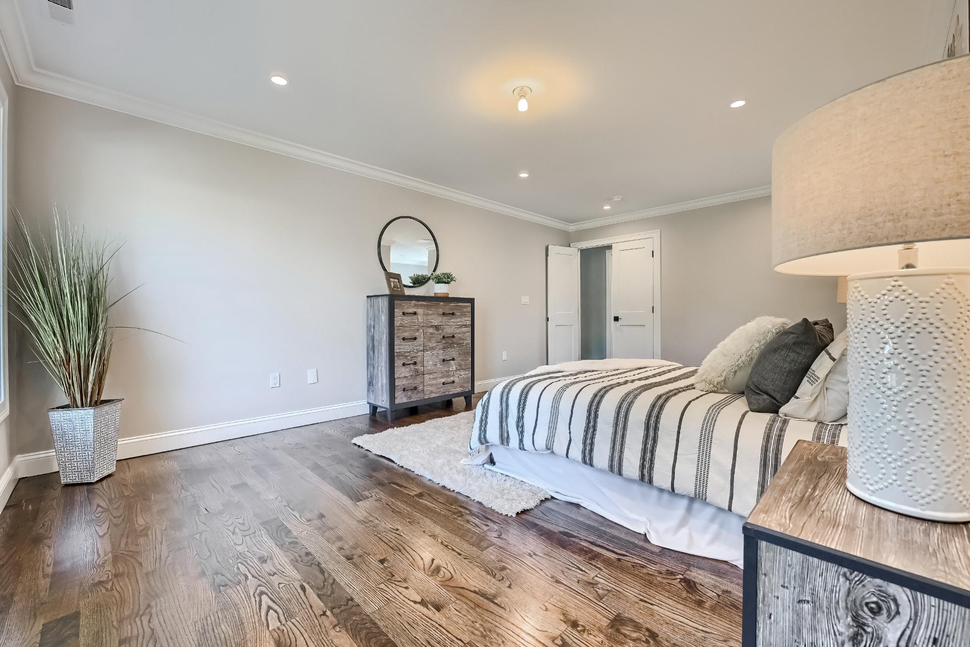 A bedroom with a bed , dresser , lamp and mirror.