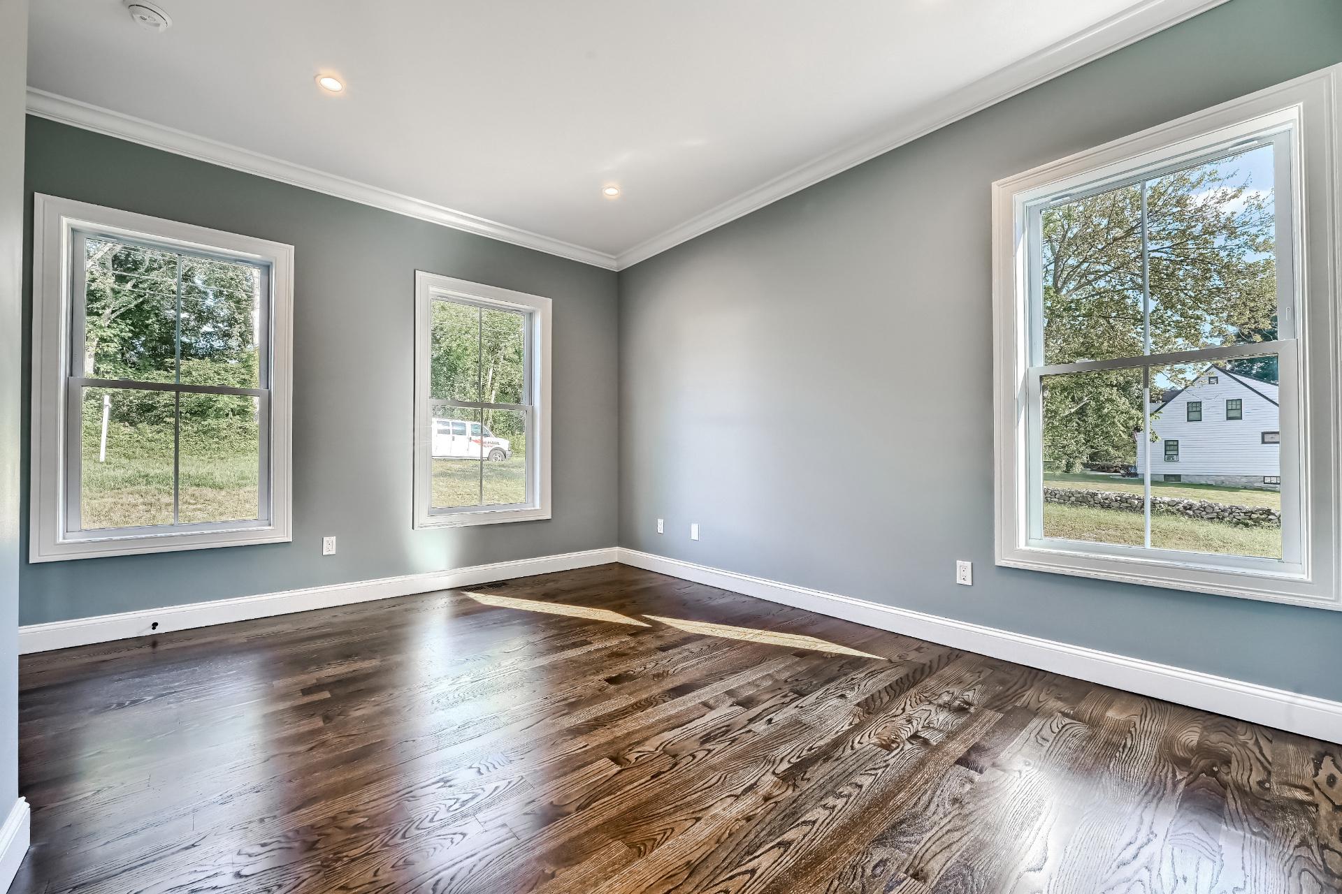 An empty living room with hardwood floors and three windows.