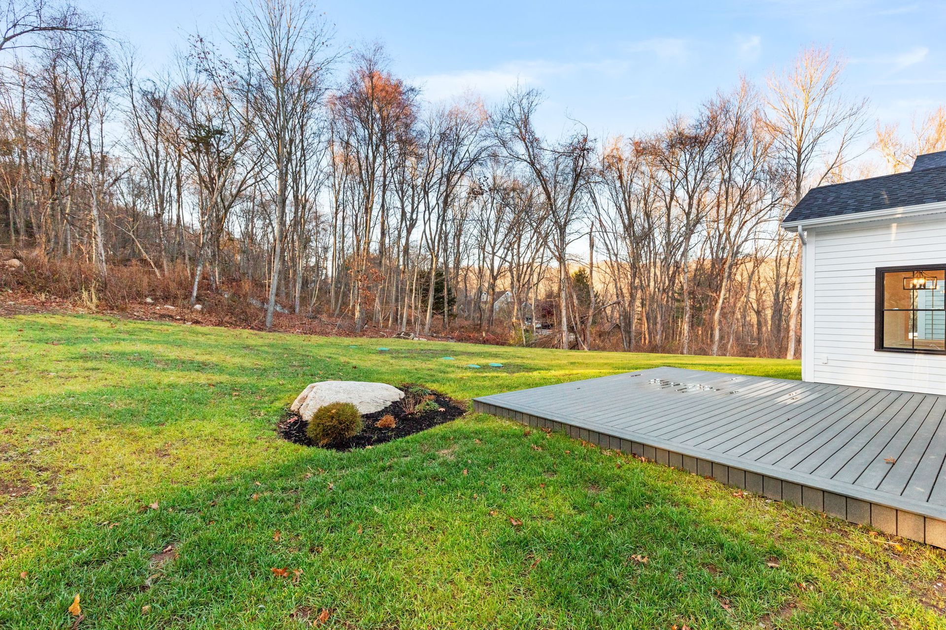 A white house is sitting on top of a lush green hillside with trees in the background.