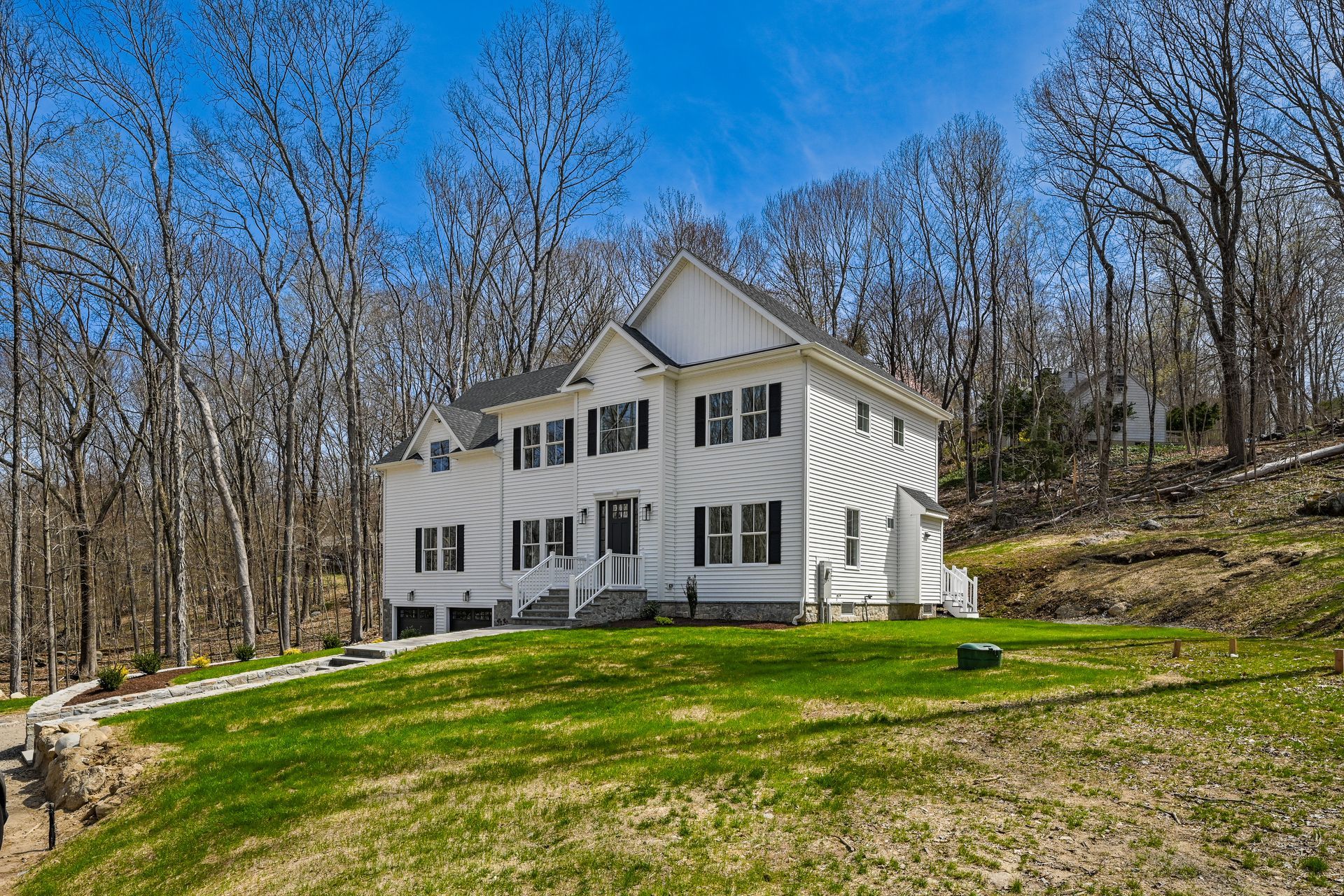 A large white house is sitting on top of a lush green hill surrounded by trees.