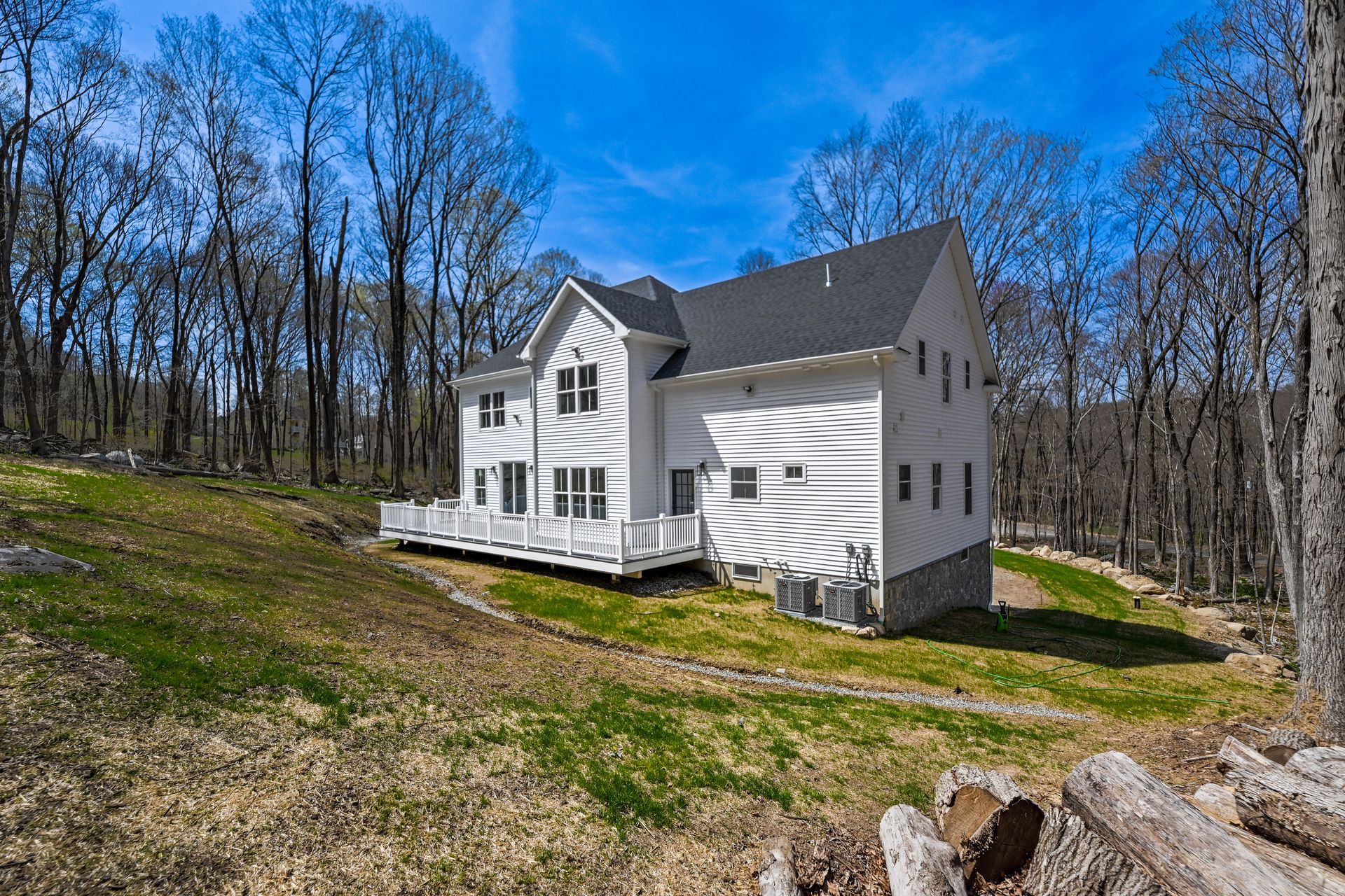 A large white house is sitting on top of a grassy hill in the middle of a forest.