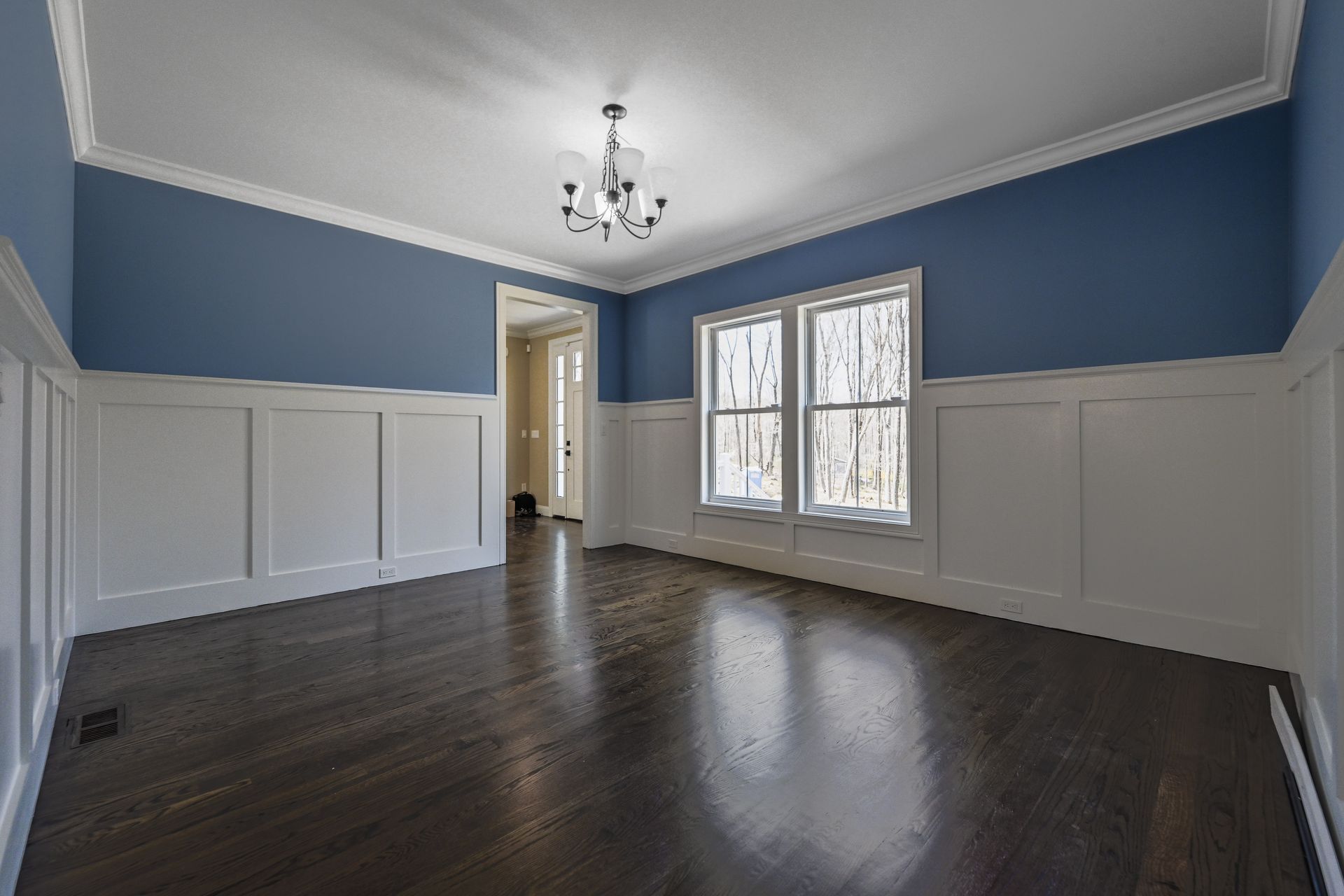 An empty room with blue walls and white trim and hardwood floors.