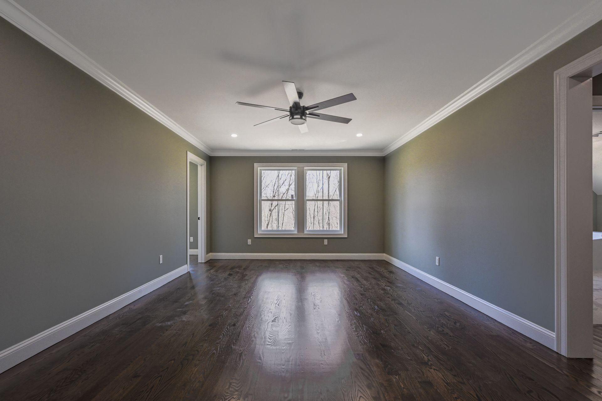 An empty living room with hardwood floors and a ceiling fan.