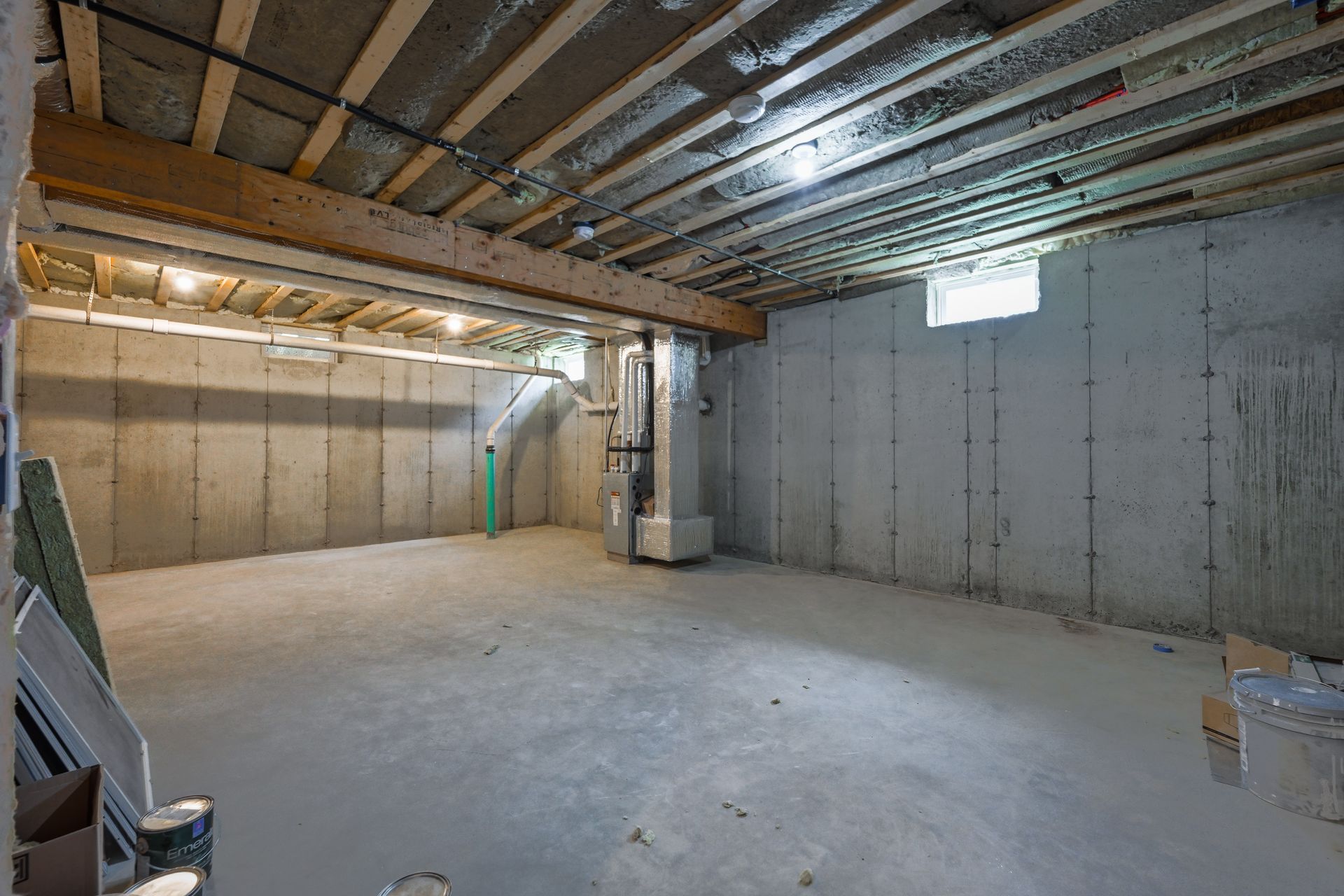 An empty basement with concrete walls and a wooden ceiling.