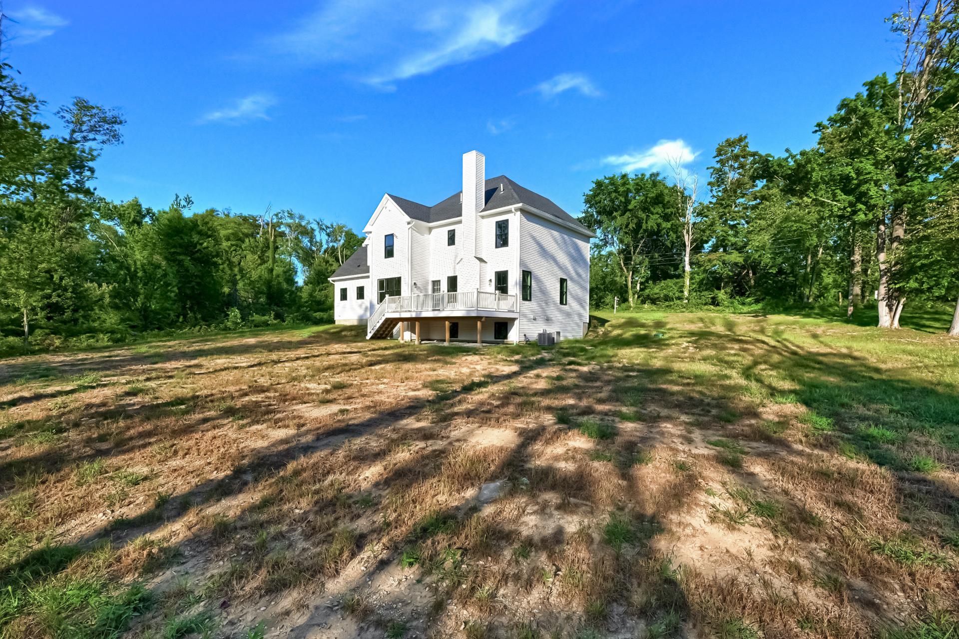 A large white house is sitting on top of a dirt field surrounded by trees.
