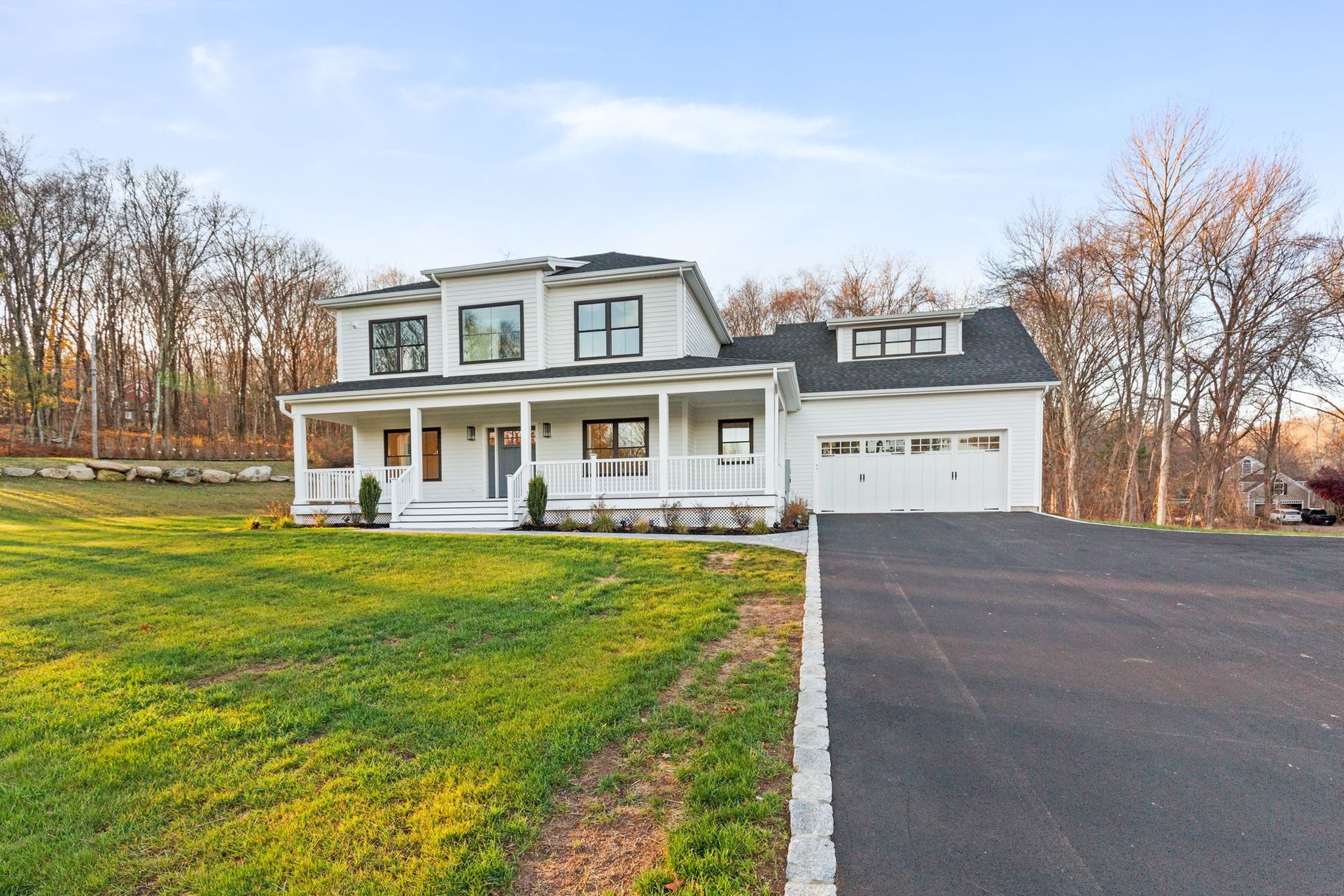 A white house with a black roof sits in the middle of a lush green field