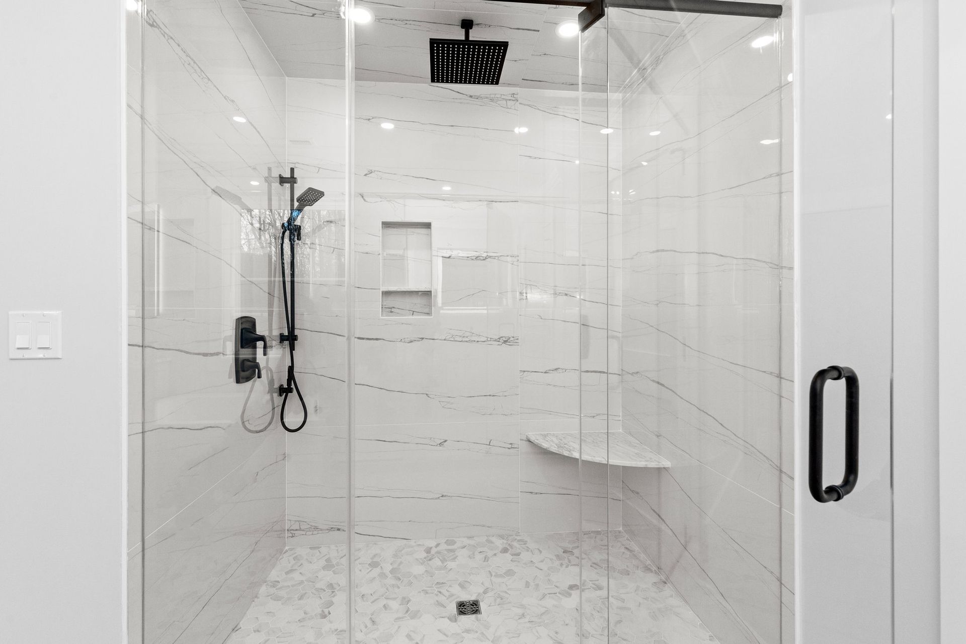A bathroom with a walk in shower with a glass door and a bench.