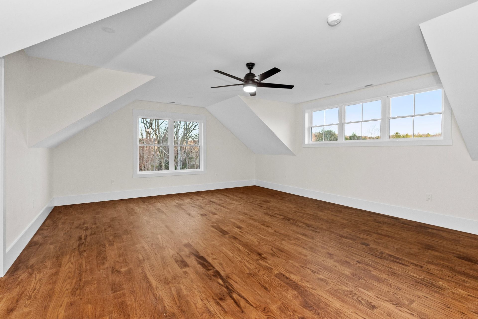 An empty room with hardwood floors and a ceiling fan