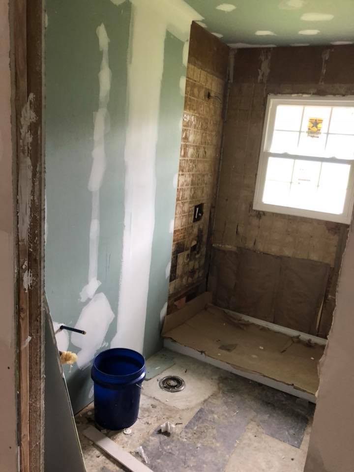 A bathroom under construction with a blue bucket and a window.