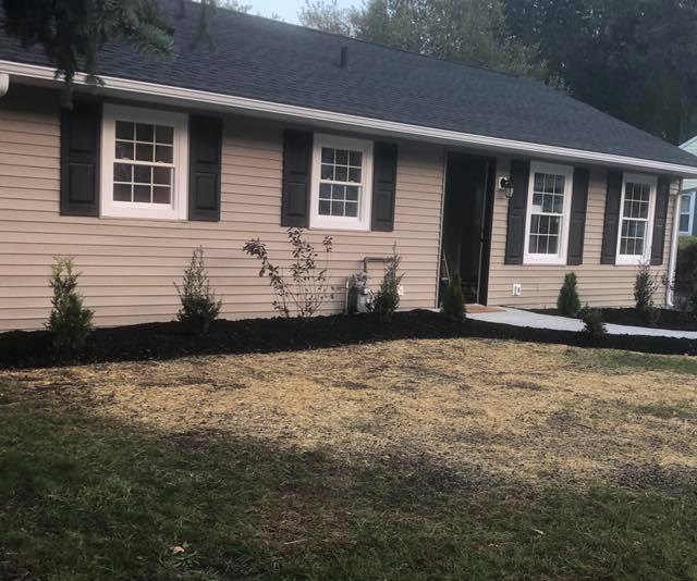 A house with a black roof and white shutters is sitting on top of a lush green lawn.