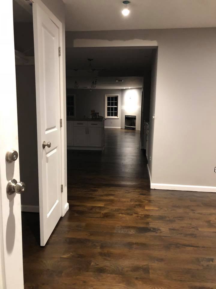 A hallway with hardwood floors and a white door leading to a kitchen.