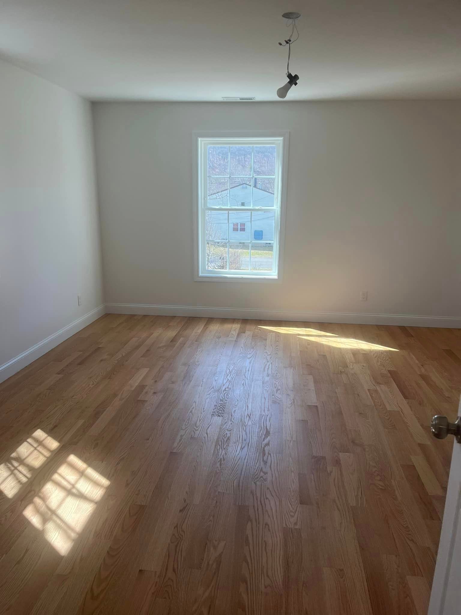 An empty room with hardwood floors and a window.