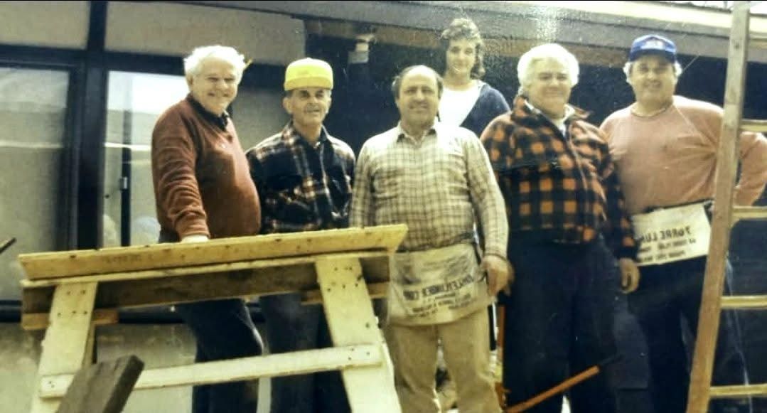 A group of men standing next to each other with one wearing an apron that says ' a ' on it