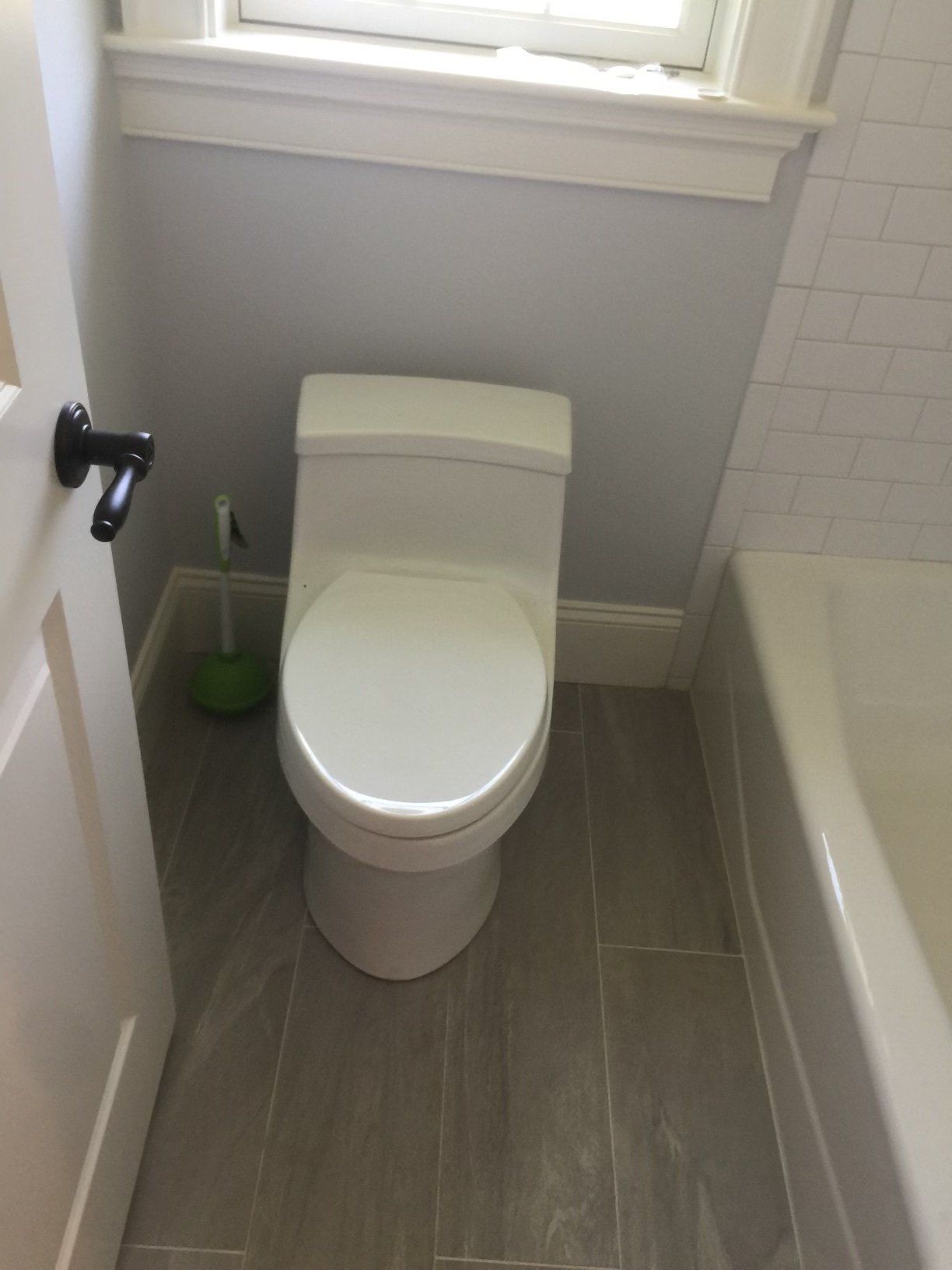 A bathroom with a toilet , bathtub and window.