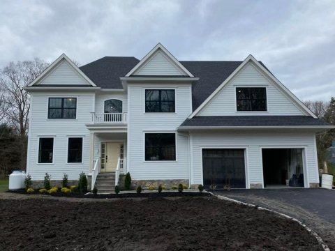 A large white house with a black roof is sitting on top of a dirt hill.