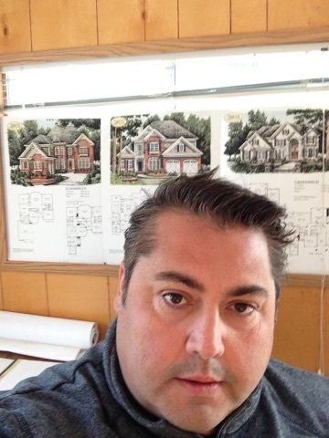 A man is taking a selfie in front of a wall with pictures of houses on it
