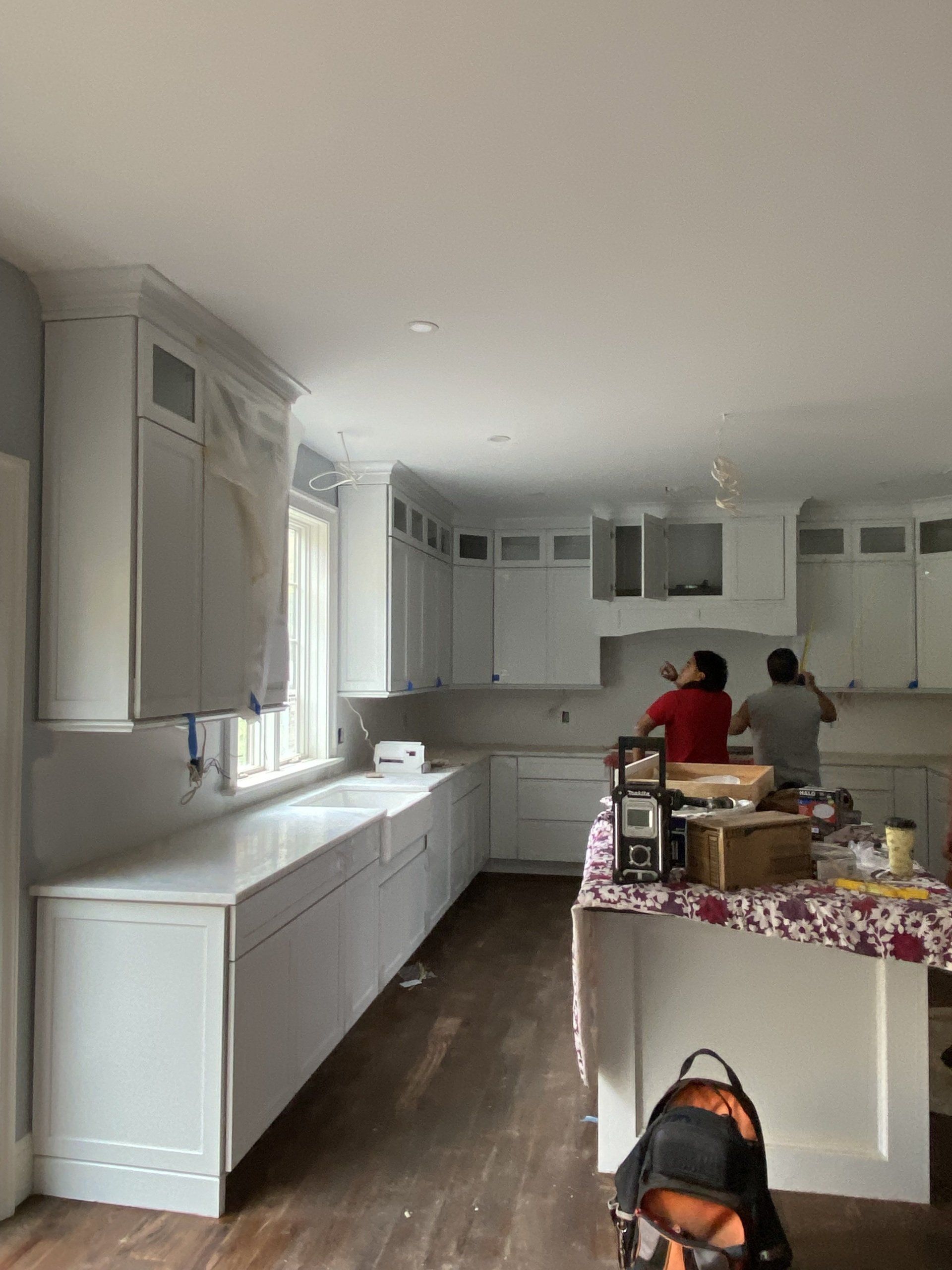 A couple of people are working in a kitchen with white cabinets.