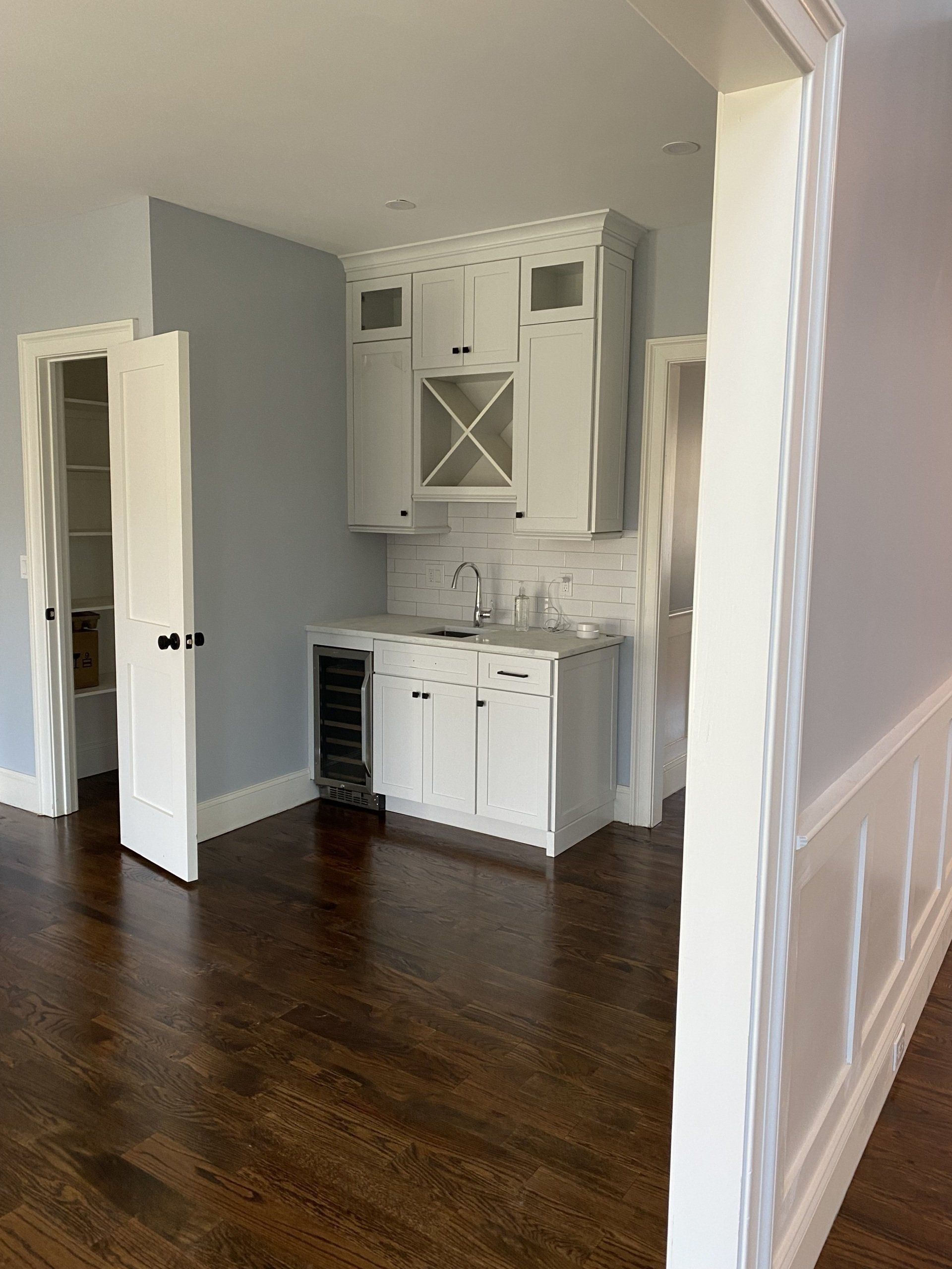 A kitchen with white cabinets , hardwood floors and a wine cooler.