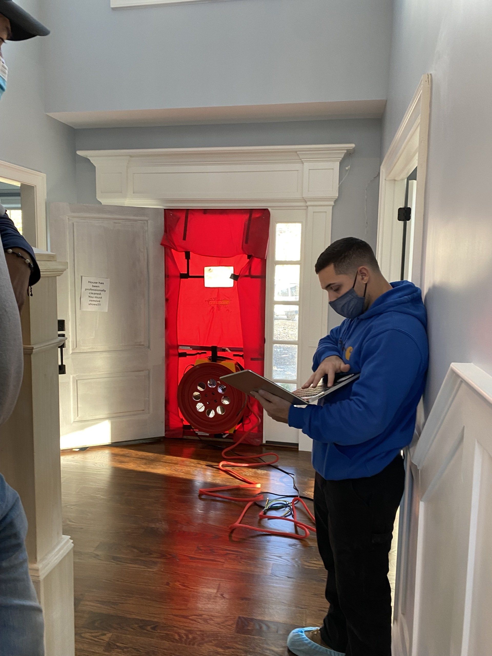 A man wearing a mask is standing in front of a red door.