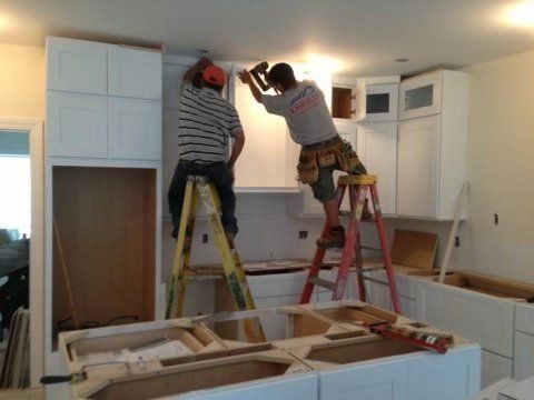 Two men are standing on a ladder working on a kitchen