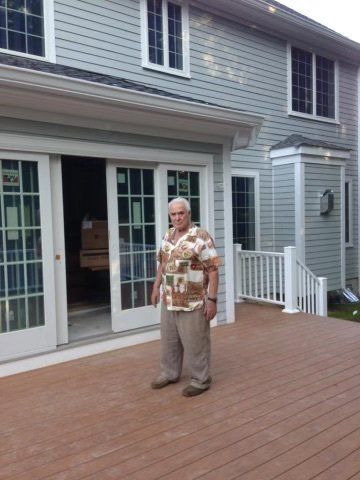 A man is standing on a deck in front of a house.