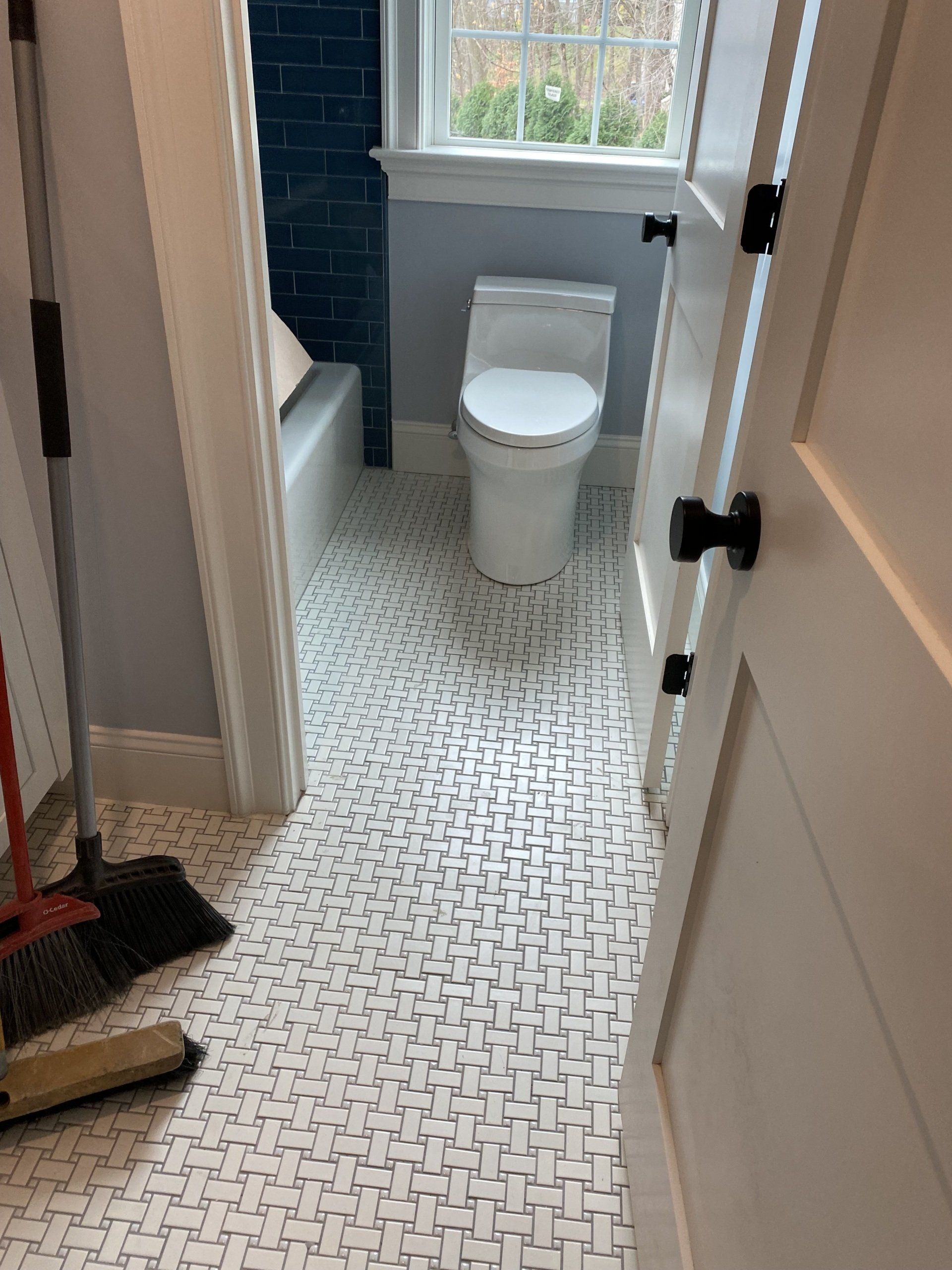 A bathroom with a toilet and a broom on the floor.