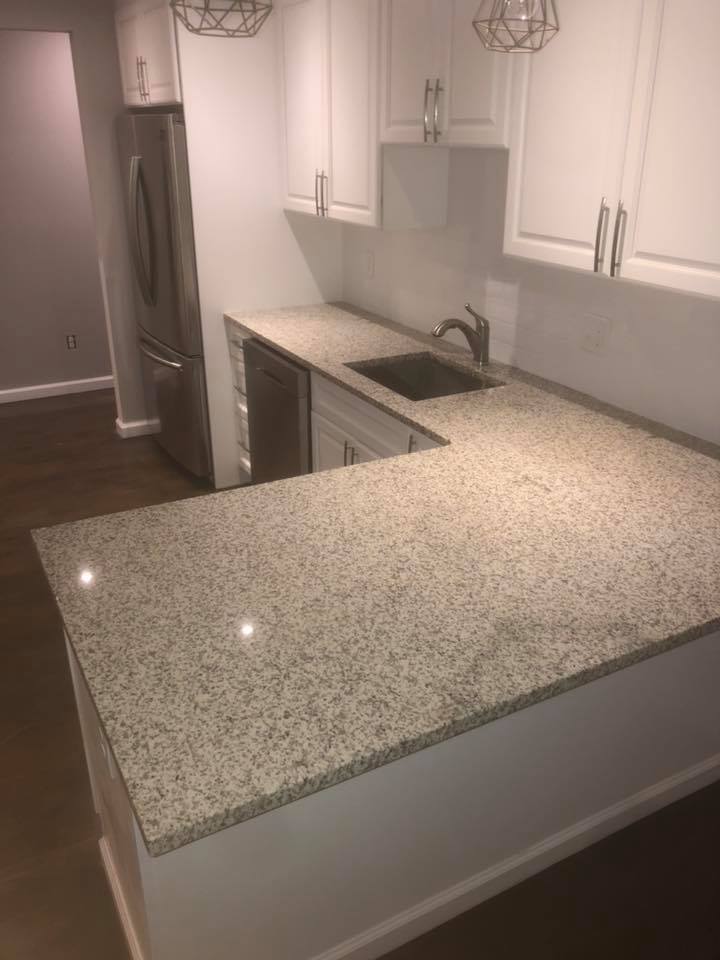 A kitchen with granite counter tops , white cabinets , a sink and a refrigerator.