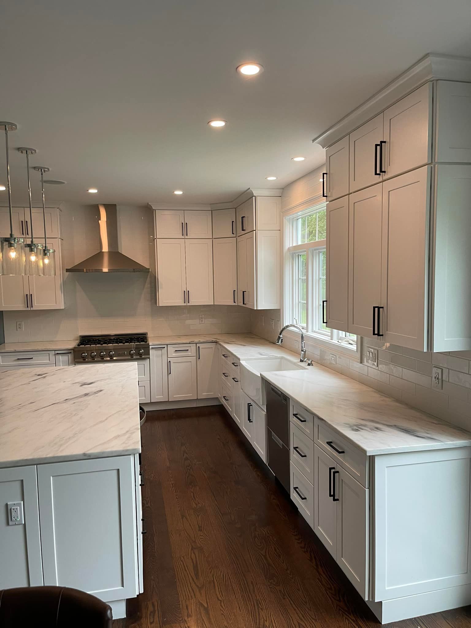 A kitchen with white cabinets and marble counter tops.