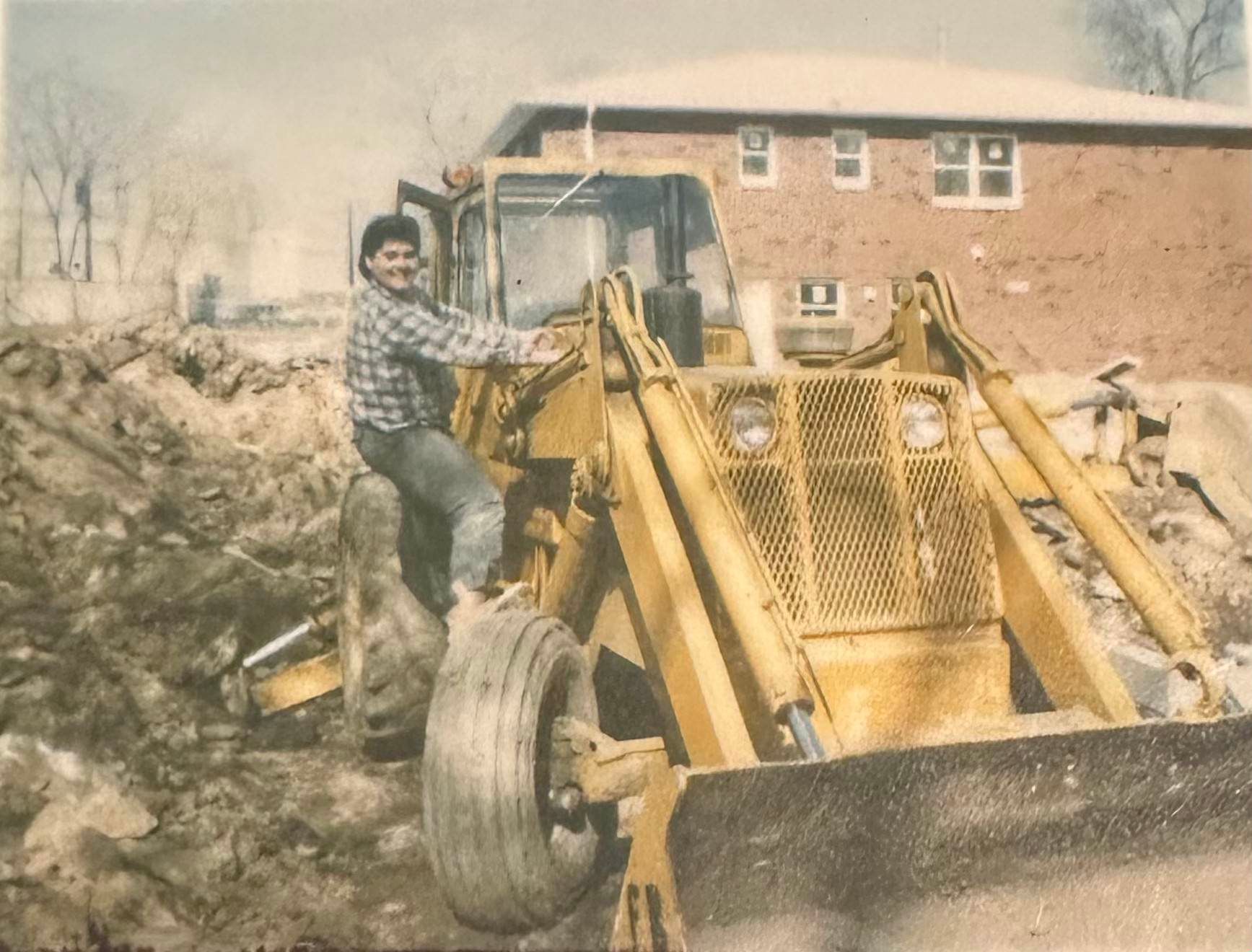 A man is driving a bulldozer in front of a brick building