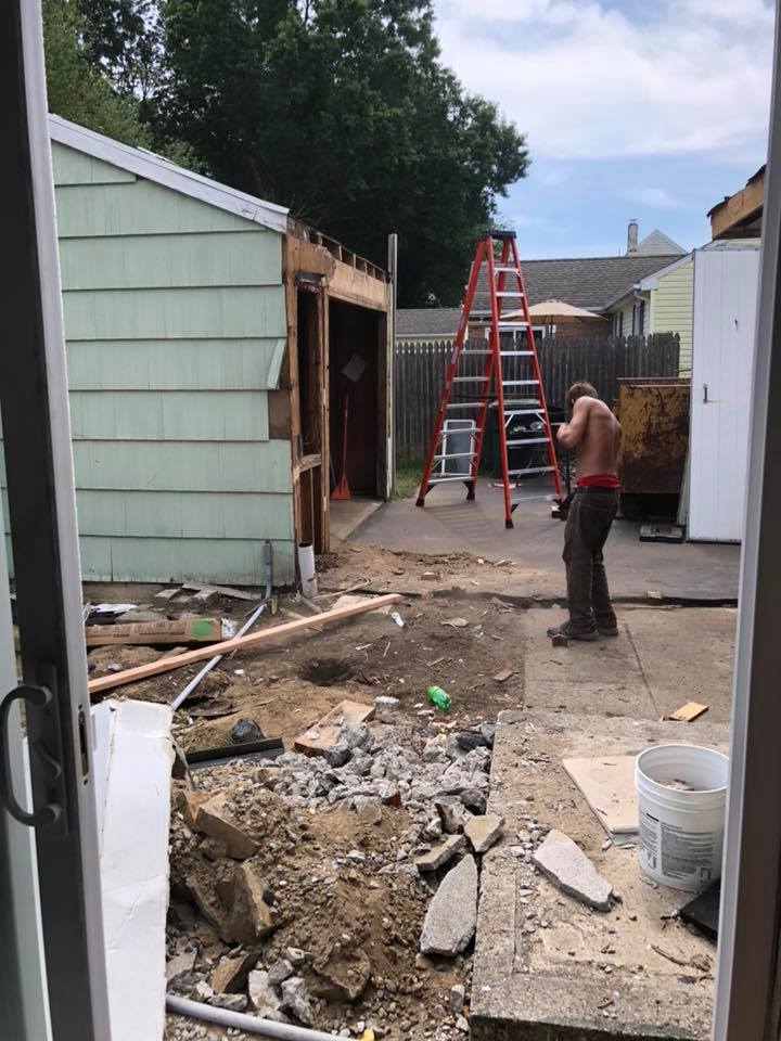 A man is standing in a yard with a ladder in the background.